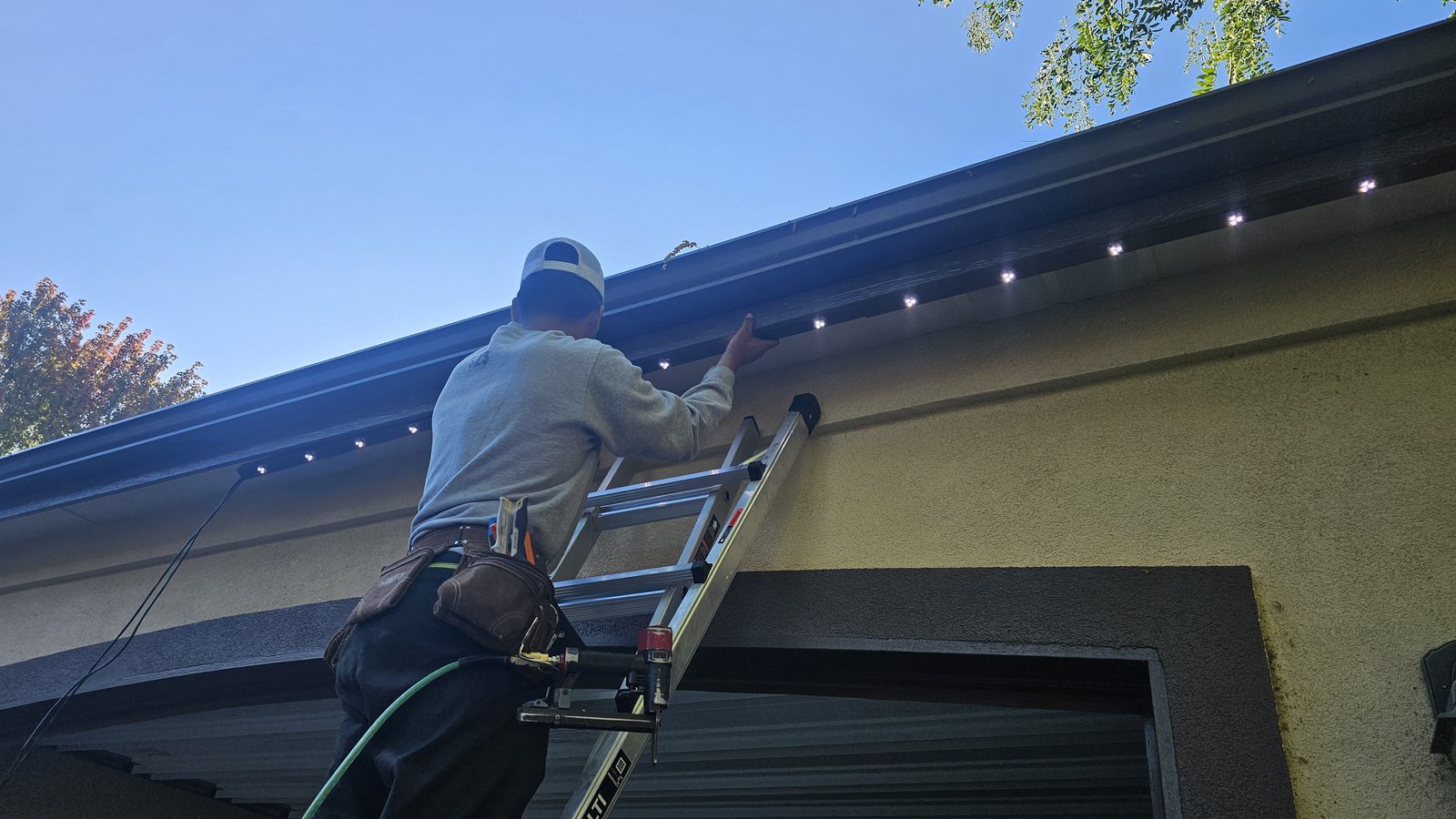 An installer fitting track along the roofline of a stucco house